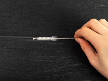 Hands Clean Glass Cocktail Tube with a Metal Brush, Glass Drink Straws Cleaning, Zero Waste Pipe on Black Background