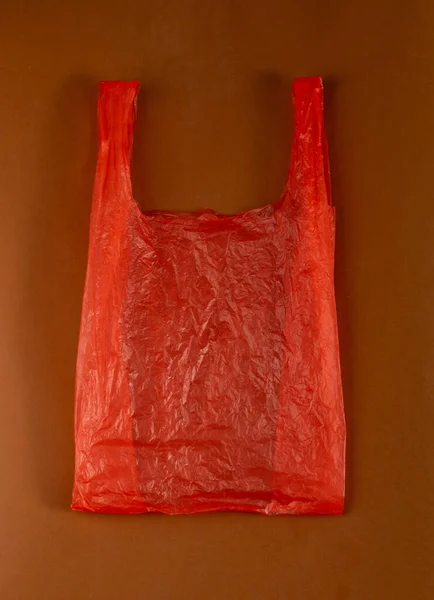ブラウン バックグラウンドの赤いプラスチック袋 ショッピングの後で粉砕されたプラスチック袋 セロファンの包装の廃棄物 使用された粉砕された使い捨て可能な袋 — ストック写真