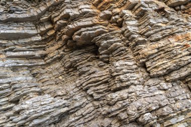 Karadağ 'ın Budva kentindeki katmanlı kaya dokusu. Engebeli yüzey gri ve kahverenginin çeşitli tonlarını gösteriyor. Görünür katmanlar ve çatlaklarla doğal oluşum, jeolojik tarih ve yapıyı vurguluyor.
