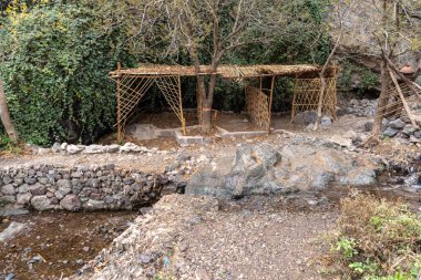 Fas 'ta dağ yürüyüşü yolunda belirsiz bir taraça, kayalık arazi ve yoğun yeşillik ile çevrili, basit ahşap yapı yürüyüşçülere gölge ve dinlenme sağlar.