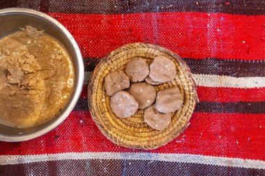 Argan yağlı macunu ve argan yağlı keki metal kasede ve örülmüş sepet kırmızı çizgili kumaş üzerinde, geleneksel üretim, toprak tonları, doğal ayar, Fas zanaatı, rustik, el yapımı, sanatsal süreç