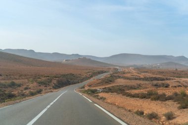 Winding road through Moroccan landscape, arid terrain, distant hills, sparse vegetation, rural area, serene drive, natural beauty, open road, gentle curves, scenic journey, tranquil view