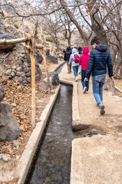 Marakeş, Fas, 10 Ocak 2024. Fas 'ta bir şelale gezisi sırasında dağ yolunda yürüyen turistler, küçük bir sulama kanalı boyunca uzanan patika, editoryal görüntü.