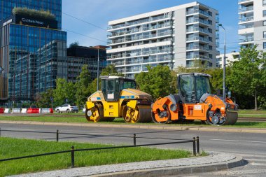 Varşova, Polonya, 19 Ekim 2023 İki asfalt silindiri park edilmiş, makineler şehir ortamında yol onarımı için hazır, modern binalar arka plan, editoryal görüntü