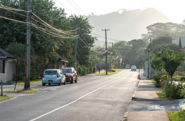 Beau Vallon, Seyşeller, 31 Ocak 2025: Güneşin doğuşunda Seyşeller 'de sakin bir tropikal cadde, park edilmiş arabalar, puslu tepeler ve yemyeşil yeşillik görüntüsü