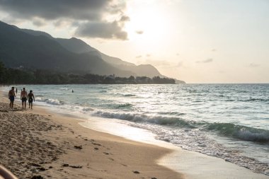 Beau Vallon, Seyşeller, 2 Şubat 2025: Turistler gün batımında Beau Vallon Sahili 'nin kumlu sahillerinde geziniyor, dalgalar kıyı şeridini hafifçe kaplıyor.
