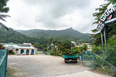 Beau Vallon, Seyşeller, 2 Şubat 2025: Kumarhane yakınlarında yeşil dağların altında bulutlu bir gökyüzü görüntüsü altında bir kamyon ve binaların bulunduğu bir park alanı.