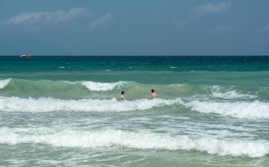 Beau Vallon, Seyşeller, 2 Şubat 2025: Sert okyanus dalgalarında yüzen iki turist, güçlü akıntılar ve uzaktaki yayın görüntüsünde görünen bir tekne