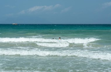 Beau Vallon, Seyşeller, 2 Şubat 2025: İki turist, ufukta görünen bir tekneyle güçlü okyanus dalgalarıyla mücadele ediyor