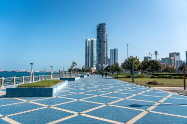 Abu Dabi, BAE, 29 Ocak 2025: Abu Dabi 'deki Corniche gezinti alanı mavi asfalt bir yürüyüş yolu, modern gökdelenler ve kıyı manzaralı editörler