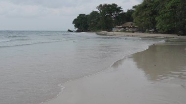 Beau Vallon plajı alacakaranlıkta bulutlu gökyüzünün altında, yumuşak dalgalar sahili kasvetli bir kıyı titreşimi ve uzak sahil ışıklarıyla yıkıyor.