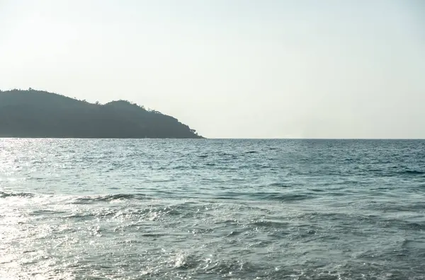 Sakin Hint Okyanusu 'nun geniş manzarası. Güneş ışığı, Berrak bir tropikal gökyüzünün altındaki yemyeşil Seyşeller adası kıyısında hafif dalgalardan yansıyor.