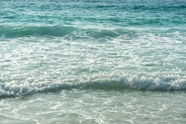 Okyanus dalgalarının yakın çekim dokusu ve güneş ışığı altındaki kumlu sahil. Turkuaz tonlar ve tropikal Seyşeller sahilinde yumuşak köpük.
