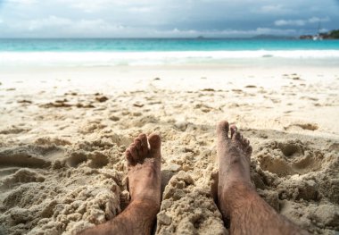 Tropikal sahildeki sıcak kumda dinlenen çıplak ayaklar yaz rahatlama, özgürlük, tatil havası, açık hava keyfi, güneşli kaçış sırasında doğal basitlik ve refahı simgeliyor.