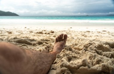 Tropikal sahildeki sıcak kumda dinlenen çıplak ayaklar yaz rahatlama, özgürlük, tatil havası, açık hava keyfi, güneşli kaçış sırasında doğal basitlik ve refahı simgeliyor.