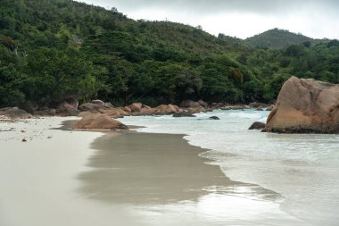 Praslin Adası, Seyşeller 'deki tropik plaj turkuvaz okyanus dalgaları, bereketli orman tepeleri, kayalık kıyı şeridi ve bulutlu gökyüzü vahşi doğayı, egzotik cenneti ve mükemmel seyahat manzarasını yakalıyor.