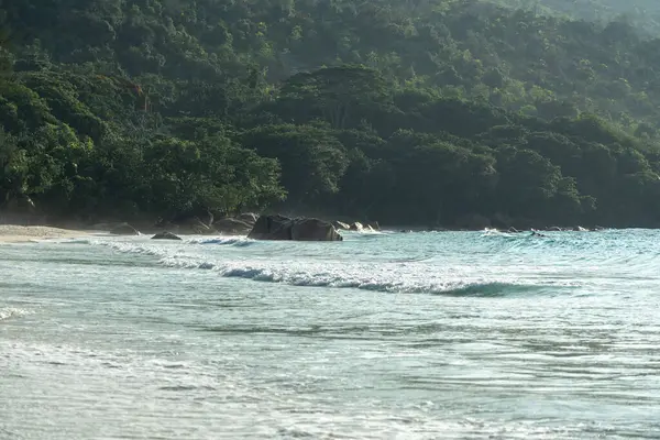 Okyanus dalgalarının yakın çekim dokusu ve güneş ışığı altındaki kumlu sahil. Turkuaz tonlar ve tropikal Seyşeller sahilinde yumuşak köpük.