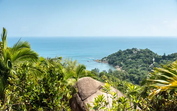 Praslin Adası, Seyşeller 'deki tropikal bir tepeden gün ortası manzarası. Hint Okyanusu, marinası ve parlak güneş ve mavi gökyüzünün altında yeşil yapraklar.