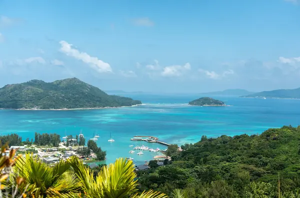 Praslin Adası, Seyşeller 'deki tropikal bir tepeden gün ortası manzarası. Hint Okyanusu, marinası ve parlak güneş ve mavi gökyüzünün altında yeşil yapraklar.