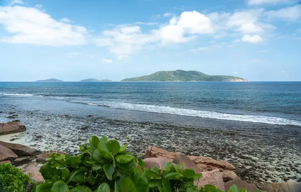 La Digue ve Praslin, Seyşeller arasındaki bulutlu gökyüzünün altında ufukta görünen granit kıyı kayaları ve okyanus dalgaları kıyı ve deniz manzaralarını gösteriyor.
