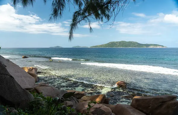 La Digue Adası, Seyşeller 'den manzara turkuaz Hint Okyanusu, beyaz mercan plajı, kıyı kayaları, yeşil bitki örtüsü ve Praslin Adası' nın uzak siluetini gösteriyor.