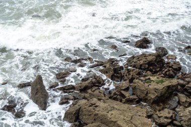 Fransa 'nın Atlantik kıyısındaki kıyı kayaları ve köpüklü dalgalar su kenarında erozyon dokusu ve deniz şekilleri gösteriyor.