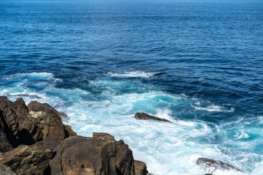 Dalga çarpması bazalt katmanları ve aşınma şekillerini görünür kırıklar ve deniz akış yapılarıyla kıyı kayaları üzerinde ortaya çıkarır.