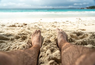 Tropikal sahildeki sıcak kumda dinlenen çıplak ayaklar yaz rahatlama, özgürlük, tatil havası, açık hava keyfi, güneşli kaçış sırasında doğal basitlik ve refahı simgeliyor.