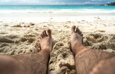 Tropikal sahildeki sıcak kumda dinlenen çıplak ayaklar yaz rahatlama, özgürlük, tatil havası, açık hava keyfi, güneşli kaçış sırasında doğal basitlik ve refahı simgeliyor.
