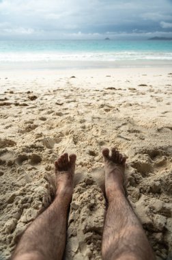 Tropikal sahildeki sıcak kumda dinlenen çıplak ayaklar yaz rahatlama, özgürlük, tatil havası, açık hava keyfi, güneşli kaçış sırasında doğal basitlik ve refahı simgeliyor.