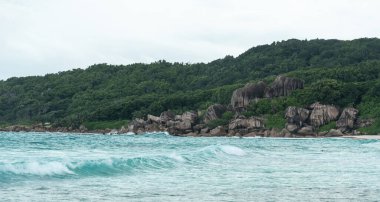 Granit kayalıklar ve yoğun orman Seyşeller 'deki La Digue adasının turkuaz dalgalarıyla buluşuyor. Kıyı şeridi, tropikal sahil boyunca doğal bir bariyer oluşturuyor.