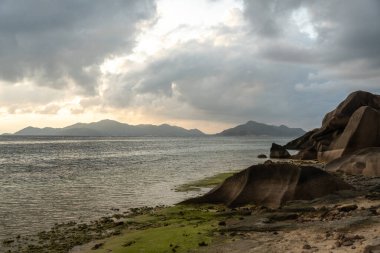 Granit kayalar ve kumlu kıyı şeridi La Digue, Seyşeller 'de okyanus dalgalarıyla buluşuyor. Uzak adalar ve dağlar tropikal bir alacakaranlık altında ufukta kaybolur.
