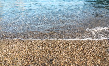 Temiz deniz suyu kumlu bir sahilde ince çakıl taşlarının üzerinden akar. Dalgalanma dokusu ve köpük doğal yatay bir pankart oluşturur