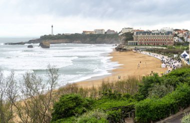 Biarritz, Fransa, 29 Mart 2024: Playa De Biarritz 'in kış havasındaki panoramik manzarası, gri fırtınalı okyanus ve uzakta deniz feneri, editoryal görüntü