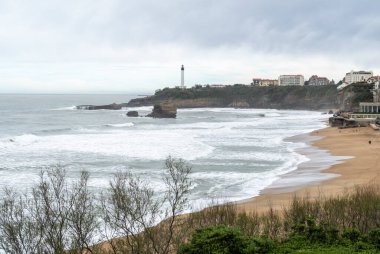Biarritz, Fransa, 29 Mart 2024: Playa De Biarritz 'in kış havasındaki panoramik manzarası, gri fırtınalı okyanus ve uzakta deniz feneri, editoryal görüntü