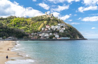 San Sebastian, İspanya, 17 Nisan 2024: San Sebastian 'ın La Concha Sahili' nin yukarısındaki dağ evleri insanların parlak gökyüzü altında Atlantik kıyısının keyfini çıkarırken,