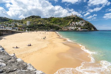 San Sebastian, İspanya, 17 Nisan 2024: La Concha Sahili 'nin altın kumu arka planda orman yamacı ve kulesi olan San Sebastian Körfezi boyunca uzanır.