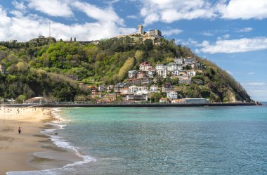 San Sebastian, İspanya, 17 Nisan 2024: San Sebastian 'ın La Concha Sahili' nin yukarısındaki dağ evleri insanların parlak gökyüzü altında Atlantik kıyısının keyfini çıkarırken,