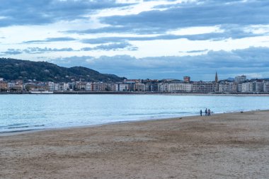 San Sebastian, İspanya, 17 Nisan 2024: San Sebastian 'ın şehir silueti, insanların sakin bir akşam sahili boyunca yürüdükleri La Concha plajına bakıyor.