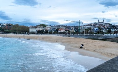 San Sebastian, İspanya, 17 Nisan 2024: San Sebastian 'da La Concha plajı boyunca akşam yürüyüşü dalgalar ve arka planda şehir silüeti, editoryal görüntü