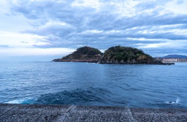 San Sebastian, İspanya, 17 Nisan 2024: Santa Clara Adası ve Monte Urgull, San Sebastian 'daki sakin Atlantik sularının karşısındaki gezinti alanından, editoryal görüntü