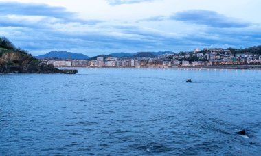 San Sebastian, İspanya, 17 Nisan 2024: San Sebastian 'ın La Concha Körfezi' ndeki ufuk çizgisinin akşam manzarası, arka planda sakin deniz ve kıyı binalarını yansıtan ışıklar, editoryal görüntü