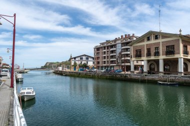 Zumaia, İspanya, 4 Nisan 2024: Zumaia 'da huzurlu bir kanal, demirlemiş tekneler, deniz kıyısındaki evler ve parçalı bulutlu bir Bask gökyüzü altındaki uzak bir köprü, editoryal görüntü içerir.