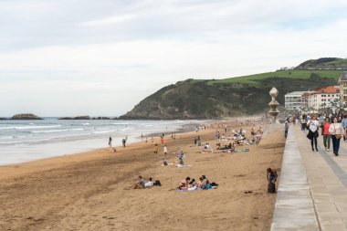Zarautz, İspanya, 4 Nisan 2024: Kalabalıklar Zarautz, İspanya 'da kumlu plajların ve gezintinin tadını çıkarıyorlar, okyanus dalgaları ve heykel manzaralarıyla. Canlı bir sahil beldesi sahnesi, editoryal görüntü.