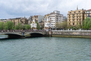 San Sebastian, İspanya, 17 Nisan 2024: Maria Cristina Köprüsü 'nün süslü heykelleri klasik binalar ve yeşil ağaçlarla çevrili San Sebastian nehri boyunca uzanır.