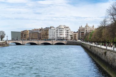 San Sebastian, İspanya, 17 Nisan 2024: Tarihi binalar, ağaçlar ve taş bir köprü ile San Sebastian nehri manzaralı bir Avrupa şehri manzarası yaratıyor,