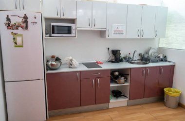 Bilbao, İspanya, 4 Nisan 2024: Elektrikli ocak, buzdolabı, mikrodalga fırın ve kurutma tezgahı bulunan kırmızı dolaplı ortak pansiyon mutfağı, editoryal görüntü