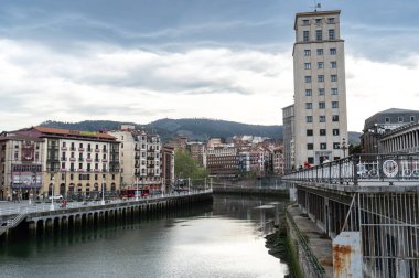 Bilbao, İspanya, 4 Nisan 2024: Bailen Kulesi 'nin çevresindeki binalar üzerinde yükselişi ve Ribera pazarı yakınlarındaki sudaki yansımaları ile Bilbao nehir kenarı manzarası, editoryal görüntü