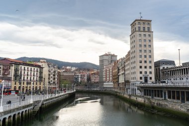Bilbao, İspanya, 4 Nisan 2024: Bailen Kulesi 'nin çevresindeki binalar üzerinde yükselişi ve Ribera pazarı yakınlarındaki sudaki yansımaları ile Bilbao nehir kenarı manzarası, editoryal görüntü