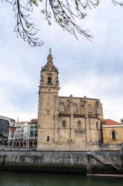 Bilbao, İspanya, 4 Nisan 2024: Eski Bilbao kasabasındaki Nervion Nehri boyunca çan kulesi ve nehir kenarındaki taş duvar ile Gotik tarzda San Anton Kilisesi, editoryal görüntü